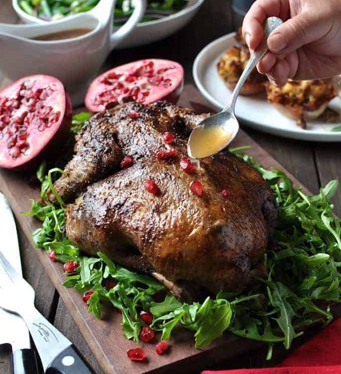 Festive Christmas Roast Duck sitting on a bed of rocket salad garnished with pomegranate seeds on a wooden board, ready for carving.