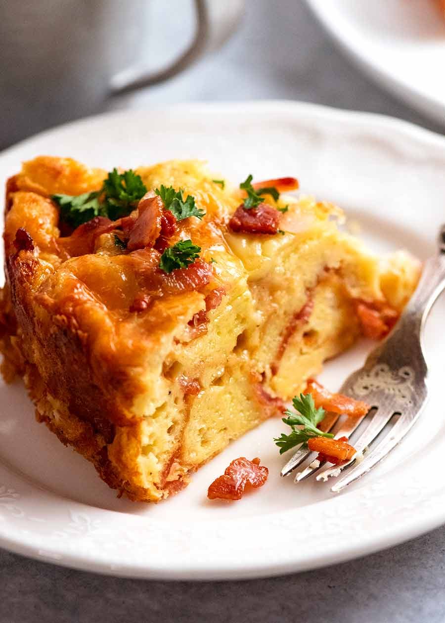 Slice of Cheese and Bacon Strata Cake - Breakfast Casserole, being eaten for breakfast