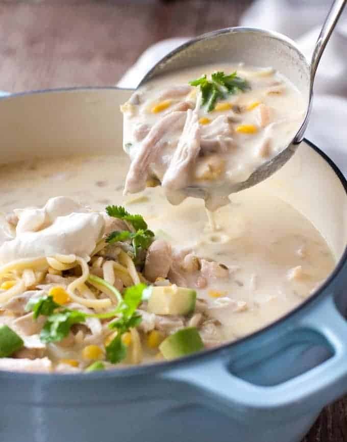White Chicken Enchilada Soup being ladled out of a pale blue casserole pot.