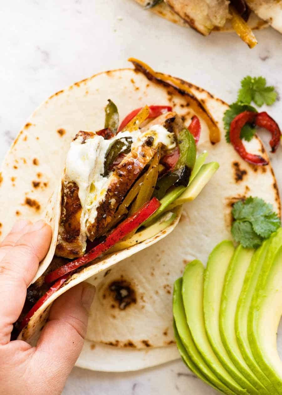 Chicken Fajitas stuffed in a warm tortilla being held but a hand, ready to be eaten.