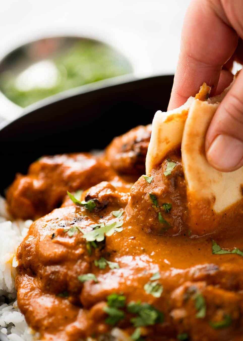 Close up of naan bread being used to scoop up some Chicken Tikka Masala.