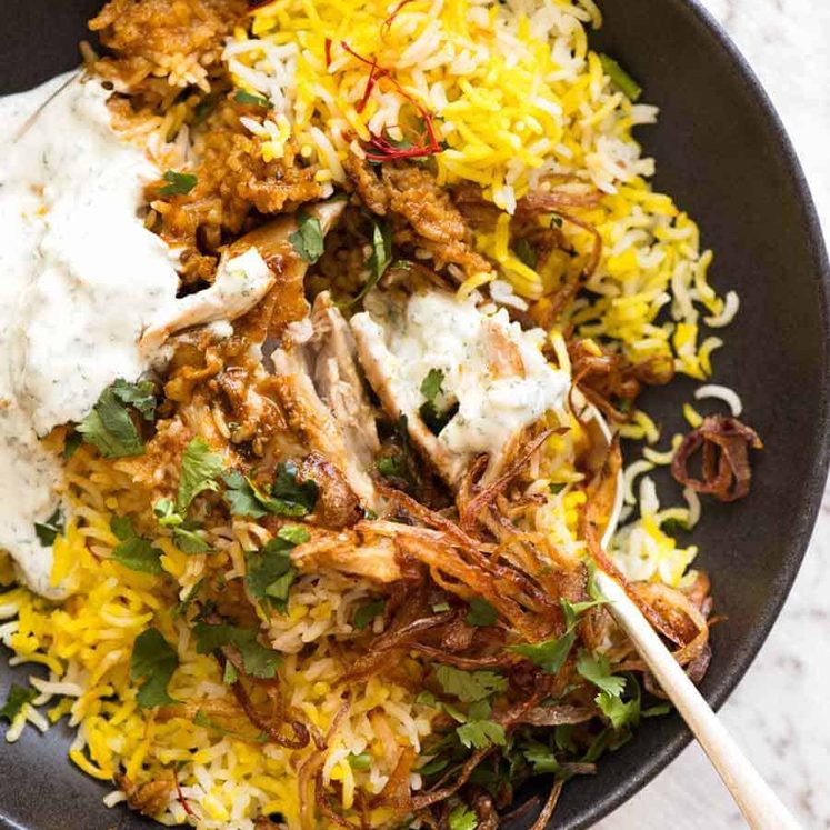 Chicken Biryani in a rustic black bowl with yellow saffron rice, garnished with crispy fried onions, coriander and minted yoghurt
