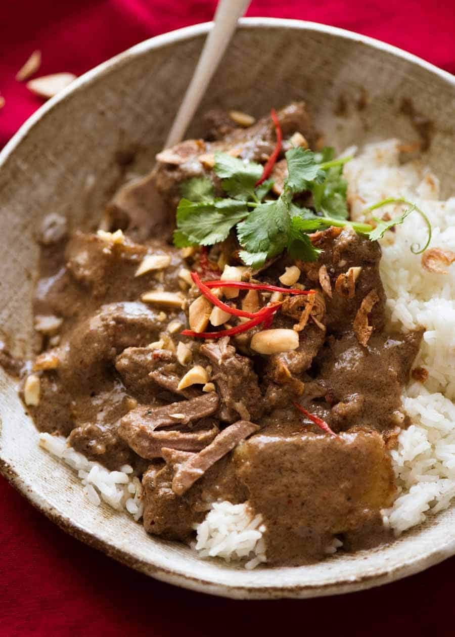 Massaman Curry over right rice in a rustic brown bowl, garnished with peanuts, fried Asian shallots and fresh red chillies, ready to be eaten
