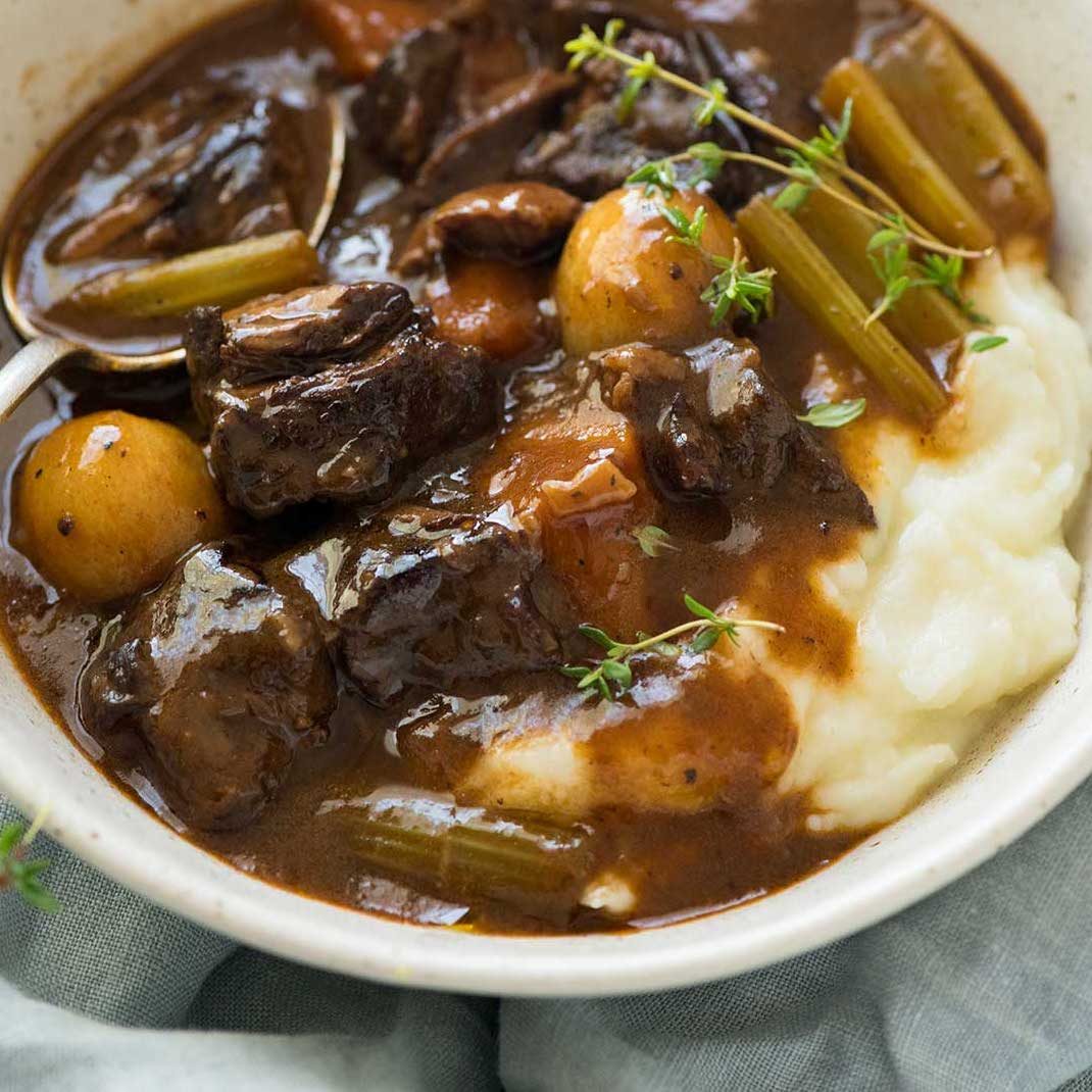 Close up of beef stew in a rich sauce served over mashed potato