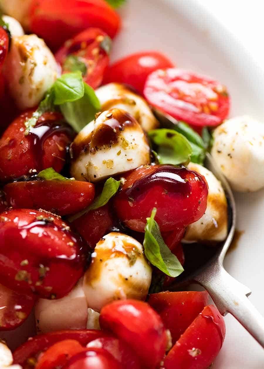 Close up of Caprese Salad with cherry tomatoes, baby mozzarella / bocconcini, basil leaves and dressed with a garlic-herb Caprese Salad dressing and drizzled with balsamic glaze.
