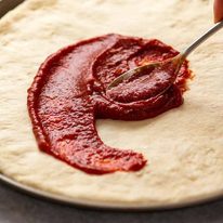 Spreading homemade pizza sauce on homemade pizza crust