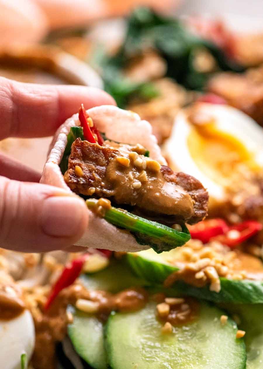 Close up of hand holding prawn cracker with Gado Gado