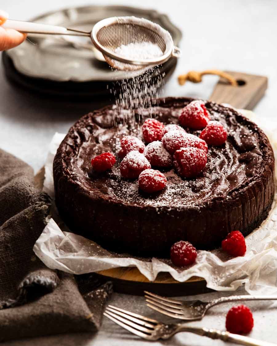 Dusting a Chocolate custard cake decorated with raspberries with icing sugar